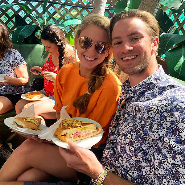 A man and a woman enjoying Miami Food Tours, holding plates of delicious food during their private culinary tour.