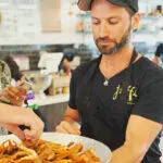 A man is handing a plate of french fries to a woman during a group tour.