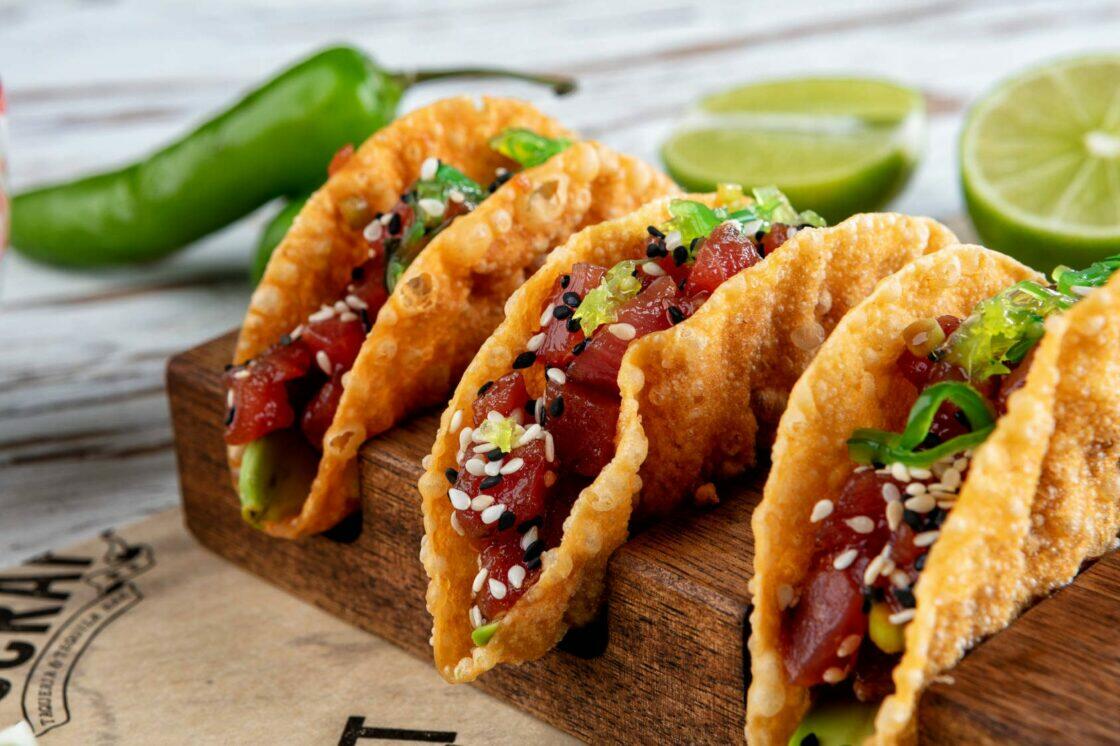 Three tacos on a wooden board with limes, perfect for Miami Food Tours.