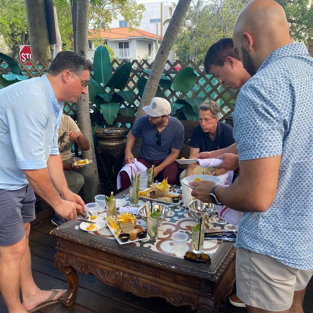 A group of men enjoying a private culinary tour with mouthwatering food at a table in Miami.