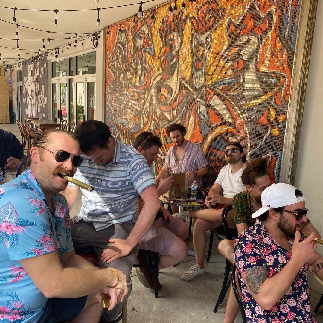 A group of people sitting at a table during a private food tour in Miami, enjoying a delicious meal in front of a vibrant mural.