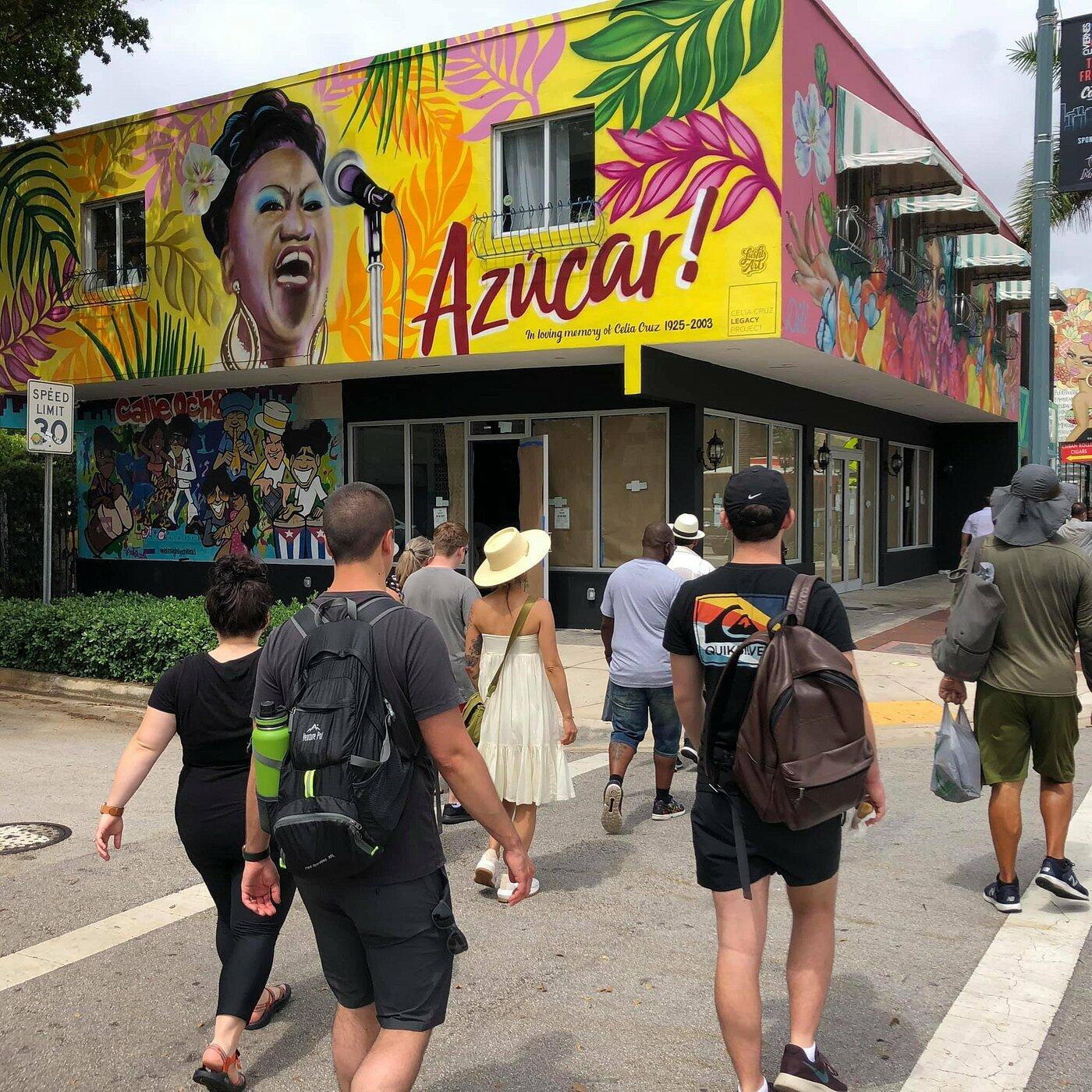 A group of people on a Miami Food Tour walk past a colorful mural on a building.