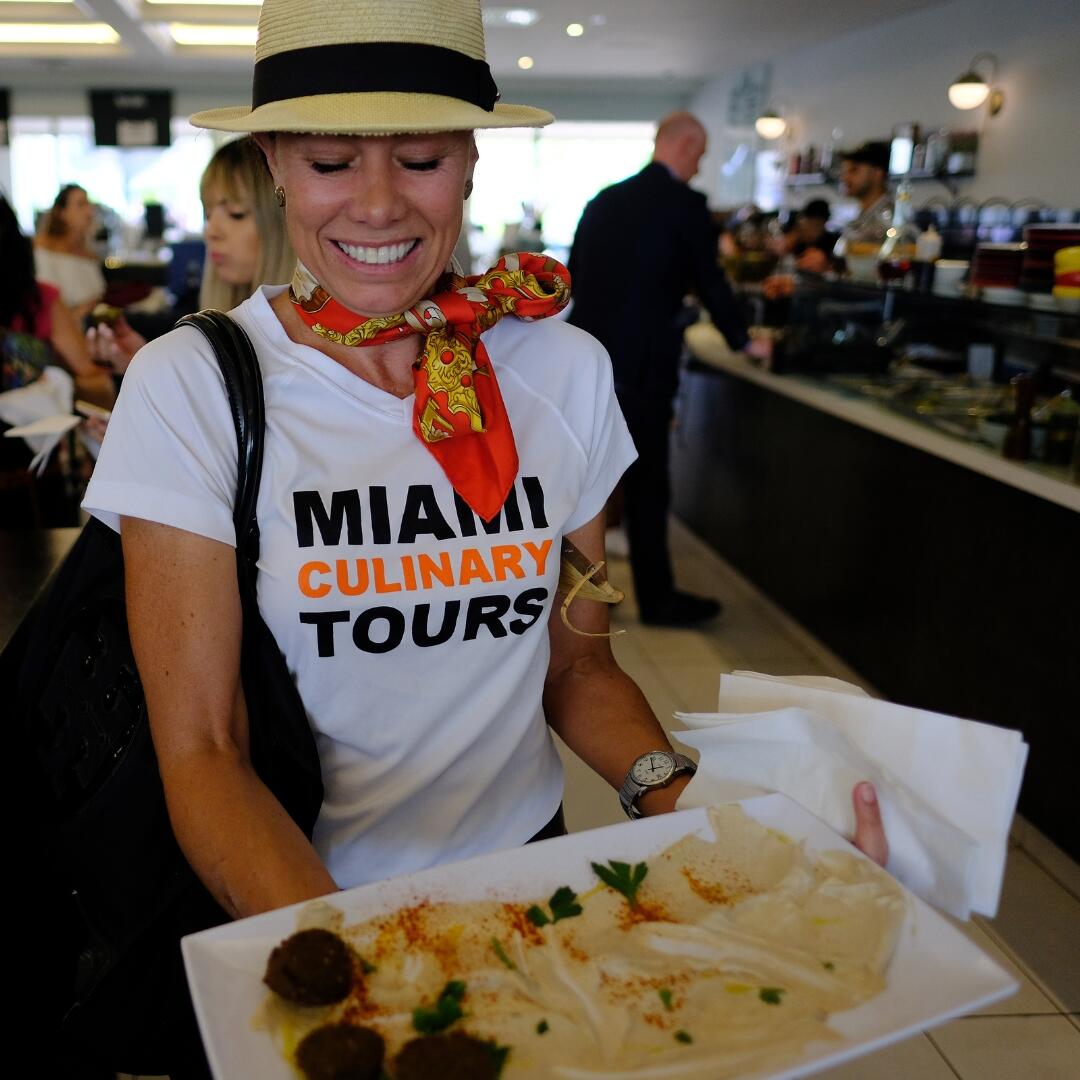 A woman holding a plate of food during a Miami Food Tour in a restaurant.