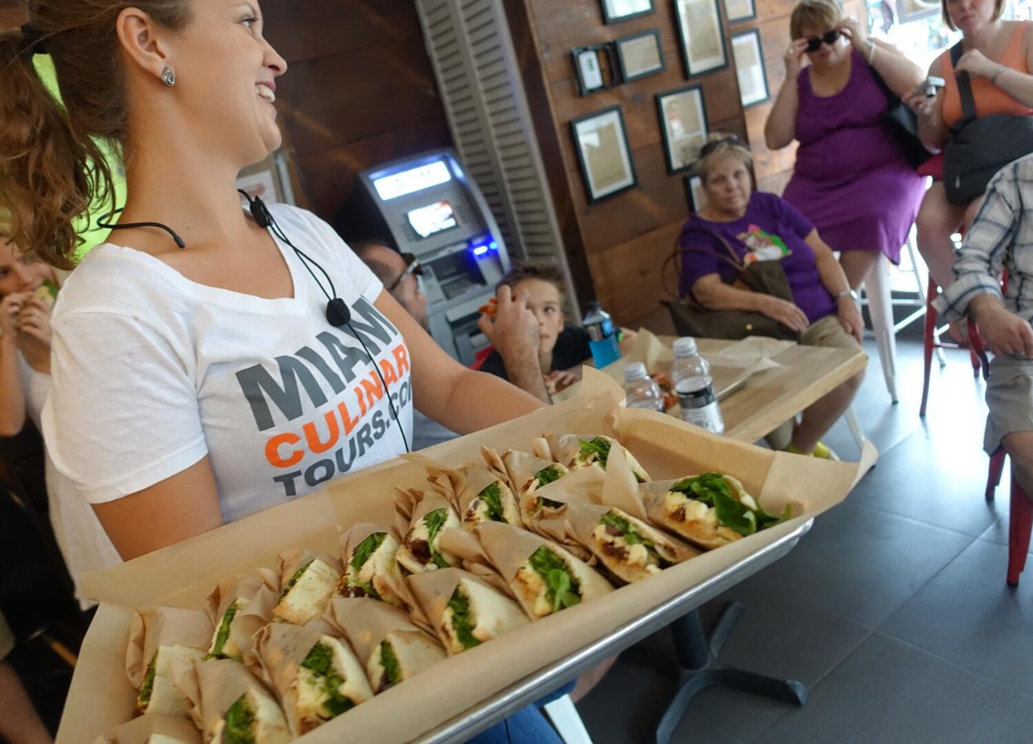 A woman is holding a tray of sandwiches during a Private Tours event.