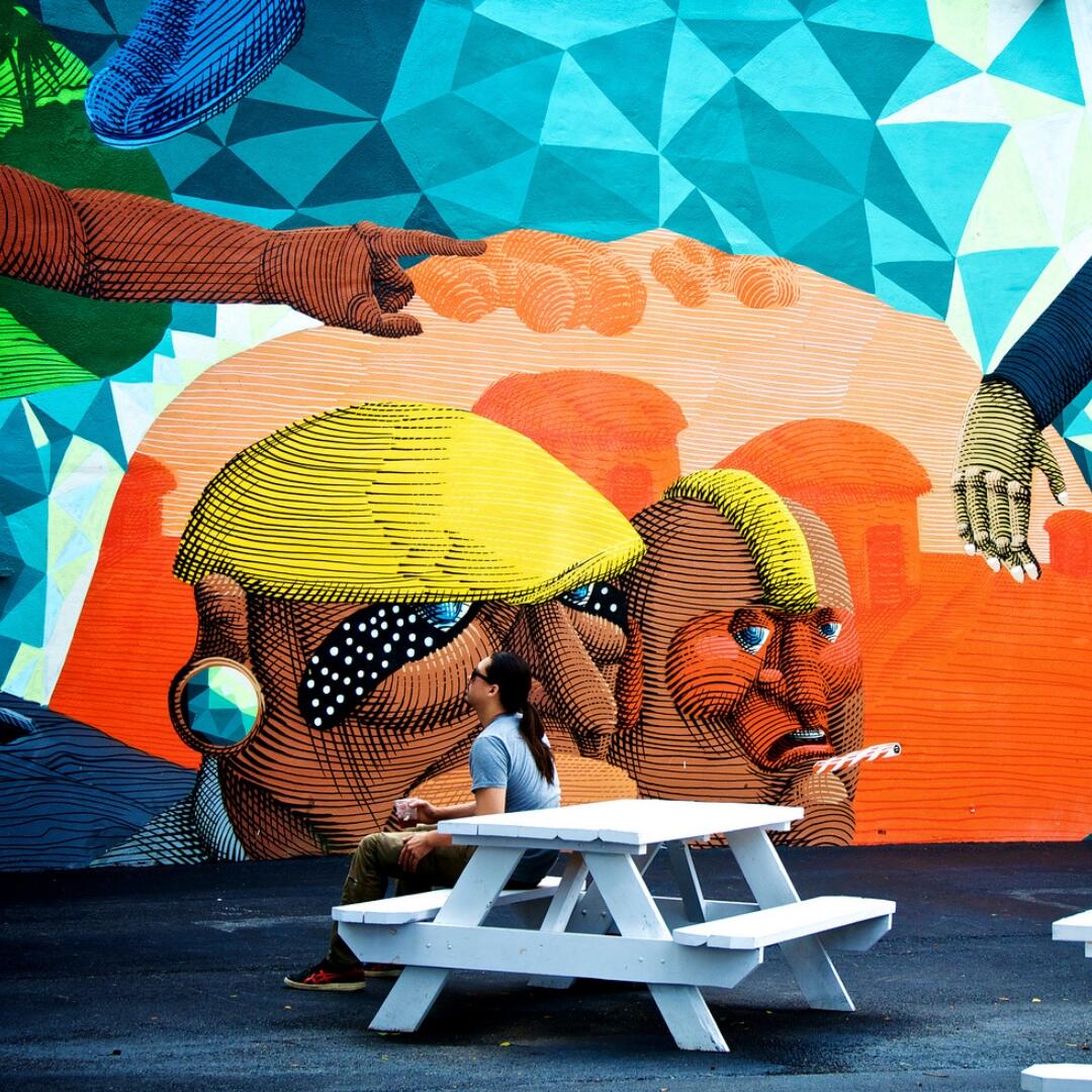 A man enjoys a Cullenary Tours experience at a picnic table in front of a mural.