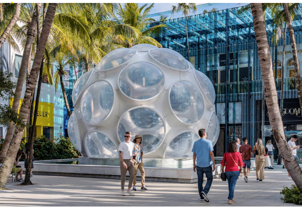 People walk past a large white geodesic dome with circular windows, surrounded by palm trees and modern buildings in the Miami Design District—an area famed for its Miami restaurants and vibrant dining guide.