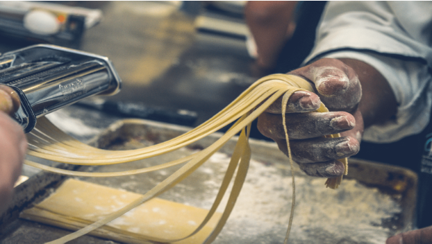 A person uses a pasta machine to cut fresh pasta dough into long noodles, holding the strands with a flour-dusted hand—a scene reminiscent of kitchens featured in top Miami restaurants.