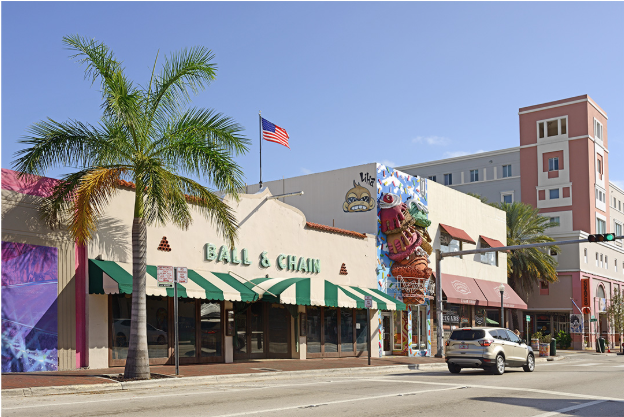 A street view in Miami’s Little Havana shows the Ball & Chain bar with a green-striped awning, palm trees, cars, an American flag, and colorful storefronts—a lively spot in any cultural guide to the area.