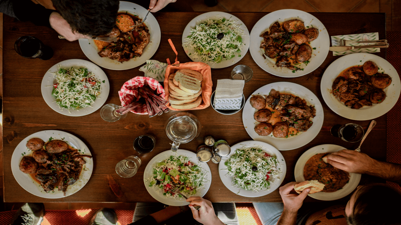 A top-down view of a wooden table set for Thanksgiving Dinner, with plates of food, salads, bread, drinks, and several people eating a meal together in Miami.