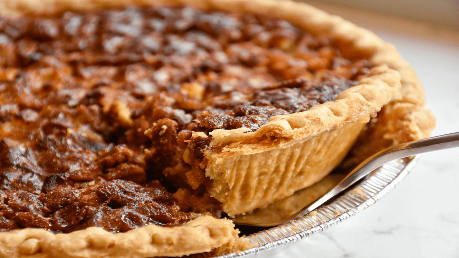 A close-up of a pecan pie with a slice being lifted out, showing the flaky crust and rich filling—perfect for your Thanksgiving Dinner in Miami.